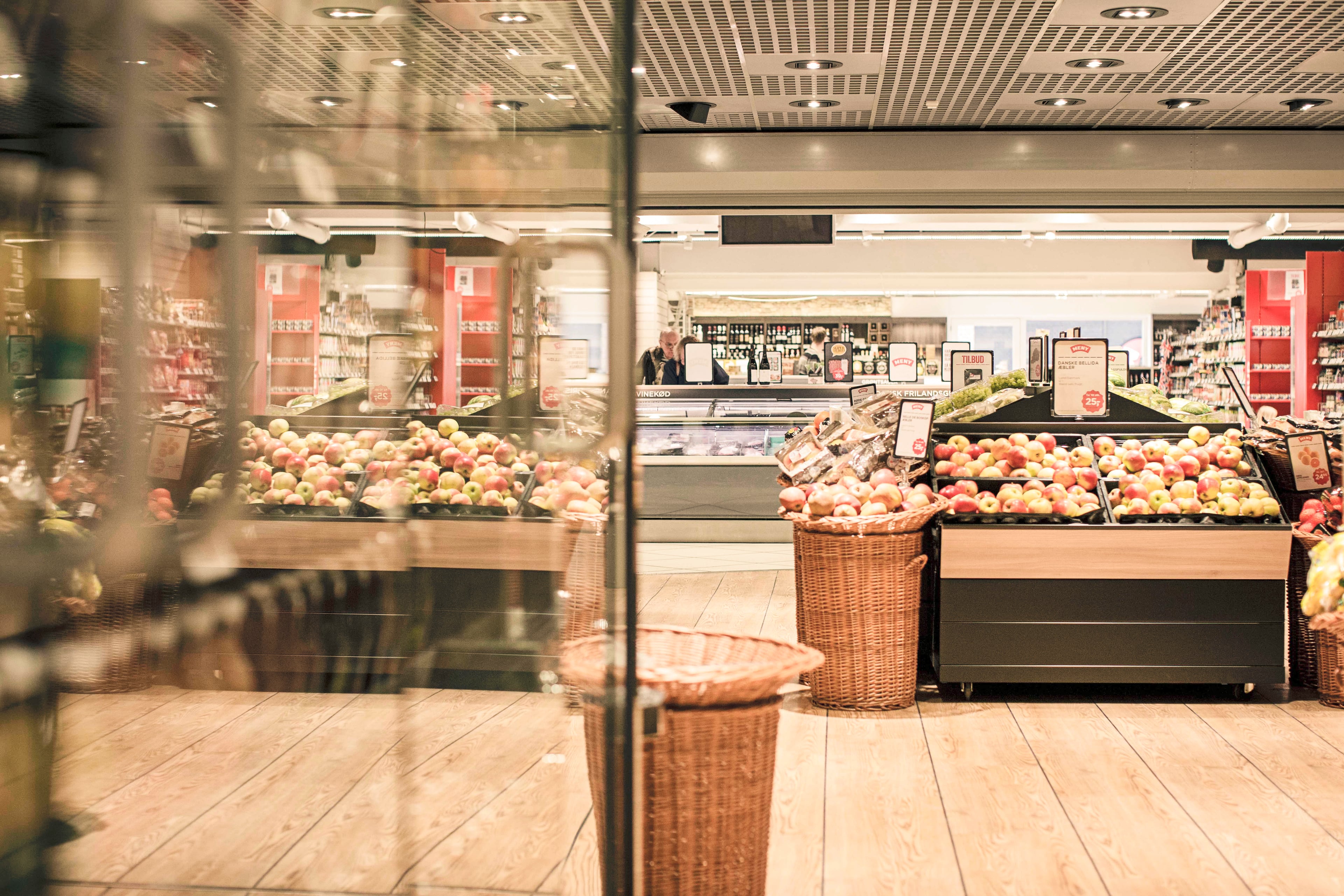 Dagrofas butik med frugt- og grøntdisplay, kurve med æbler og løg, butiksdisk og hylder med varer