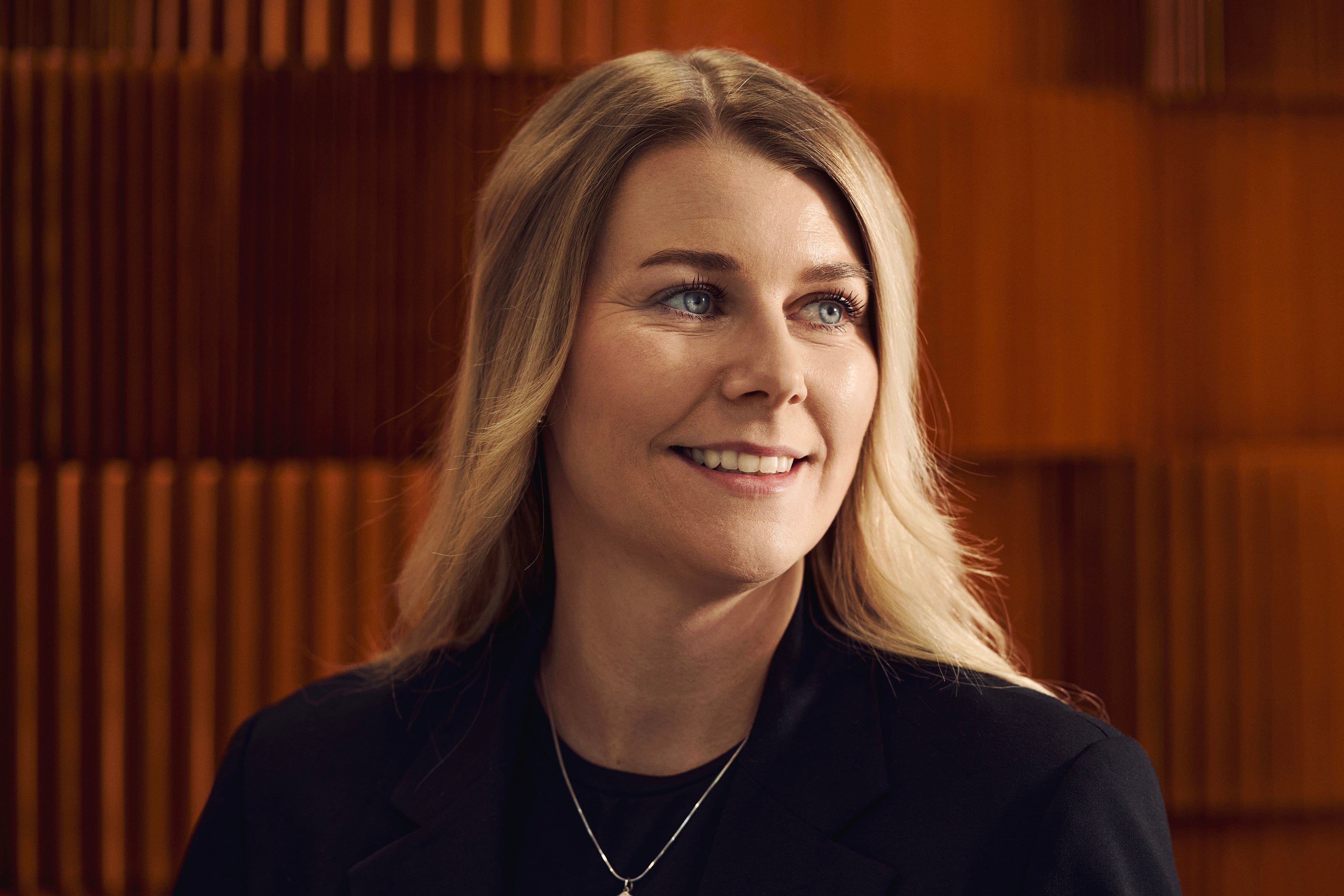 Kvinde med lyst hår smiler mod kameraet foran foran orange vægpanel