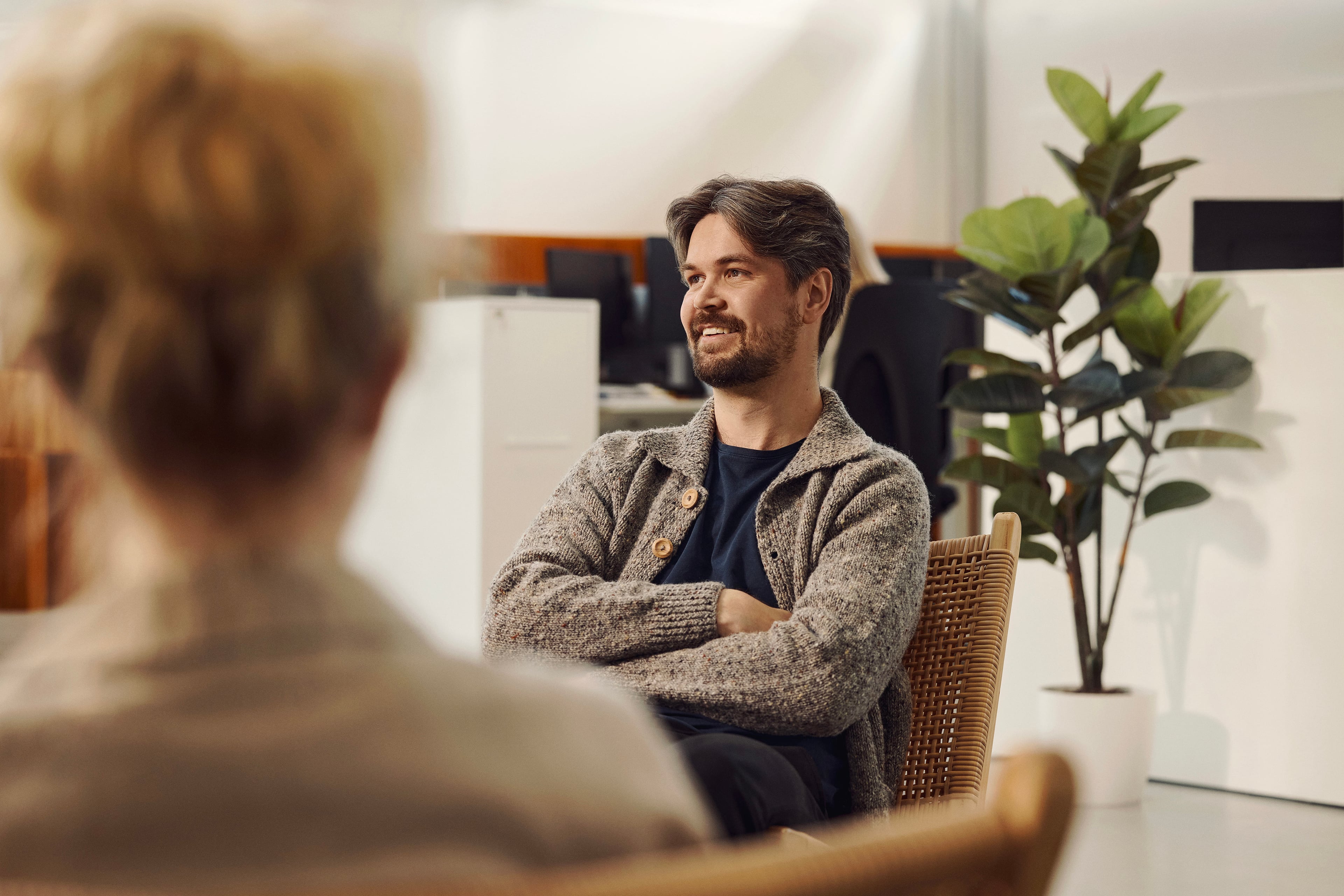 Mand i samtale med kvinde på kontor med plante og møbler i baggrunden