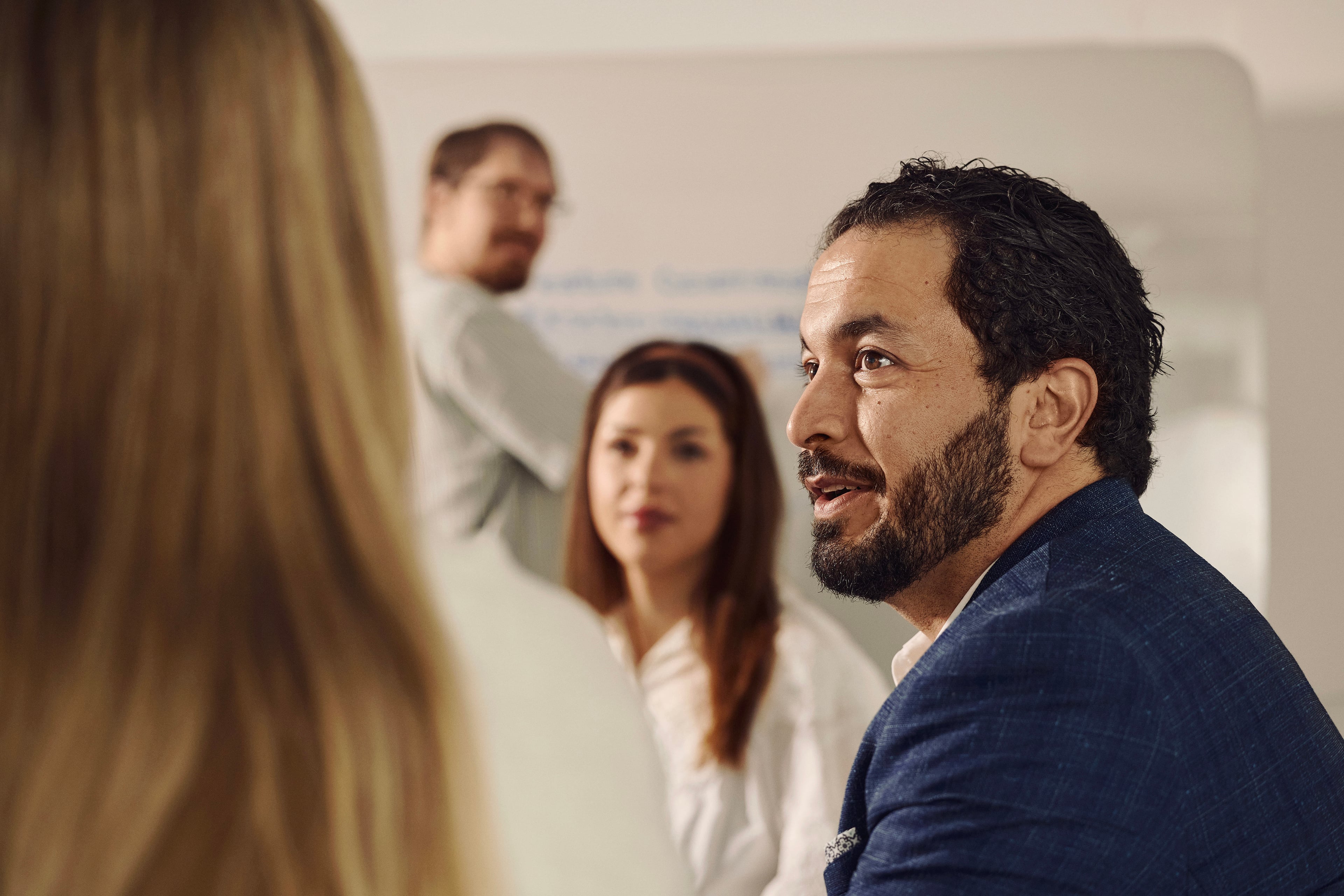 Mand i møde lytter til kollega, fire personer i mødelokale